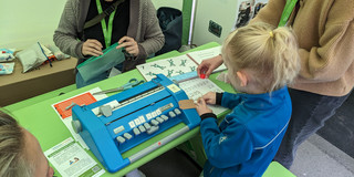 Ein Kind steht an einem Basteltisch neben einer Braillemaschine